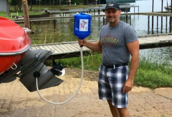 Man holding a homemade water dispenser at a lakeside.